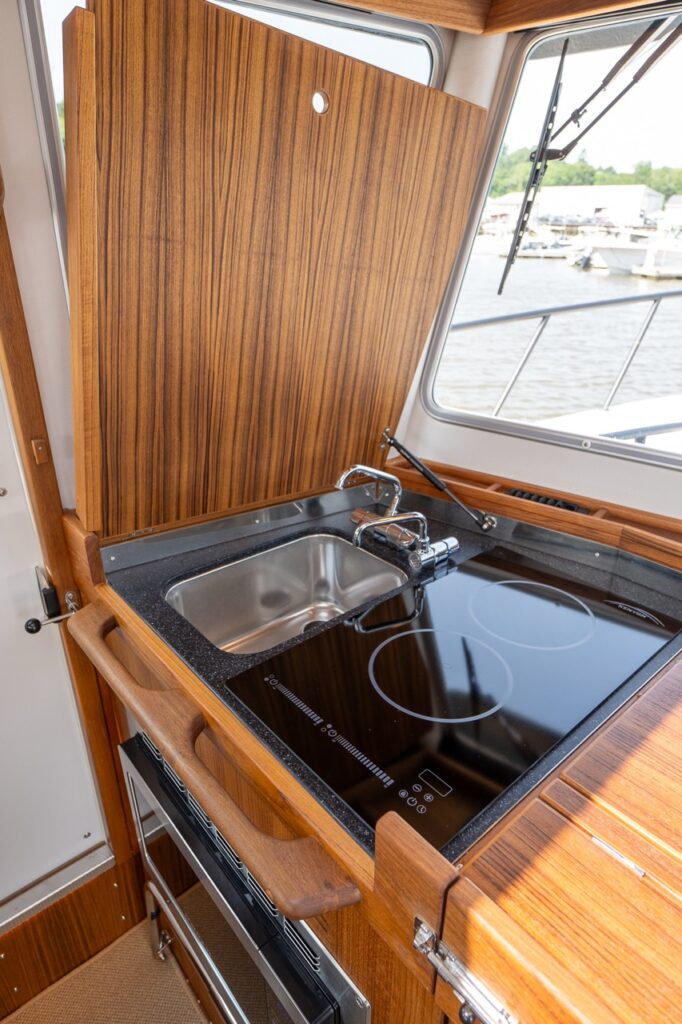 Targa 32 pilot house galley with lid open, showing stainless sink and induction cooktop beneath a hinged wood cover.
