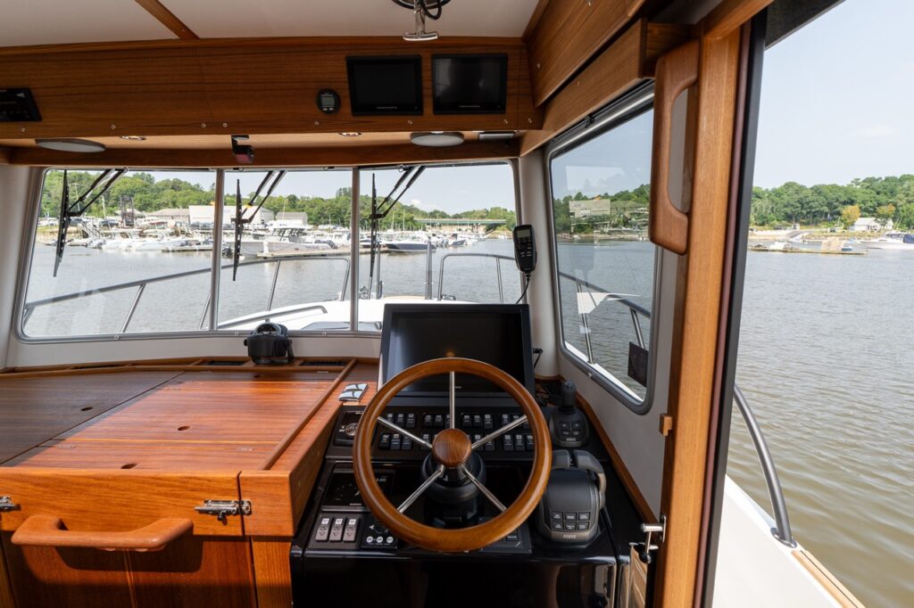 Wide view of the Targa 32 pilot house helm with wooden steering wheel, navigation displays, and panoramic forward windows.