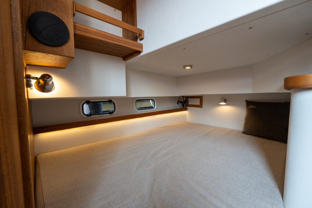 Double aft berth aboard the Targa 32 featuring a wide sleeping surface, warm teak trim, integrated reading lights, portlights, and soft ambient lighting.