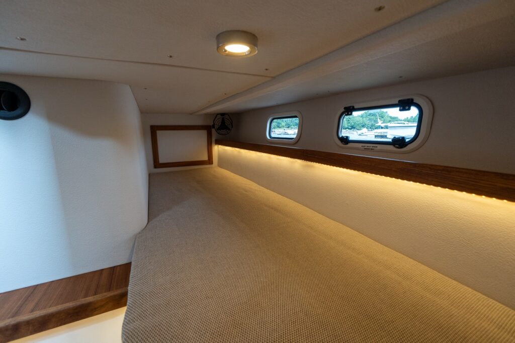 Aft single berth aboard the Targa 32 featuring a long upholstered sleeping surface, warm accent lighting, small portlights, and a clean, practical layout.