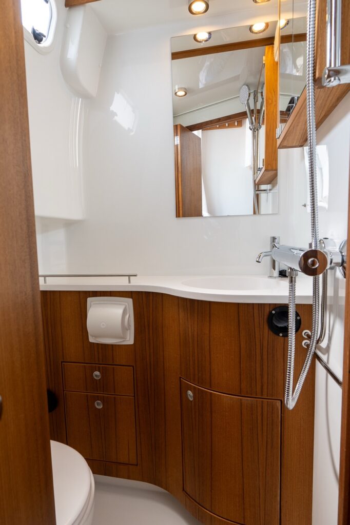 Head compartment aboard the Targa 32 featuring warm teak cabinetry, integrated sink, mirror storage, and a separate shower in a bright, well-finished space.
