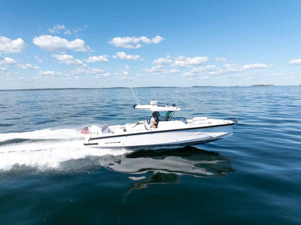 Side profile of an Axopar 29 CCX center console running on plane across calm water under a blue sky, with the Cross Top and a trailing wake.
