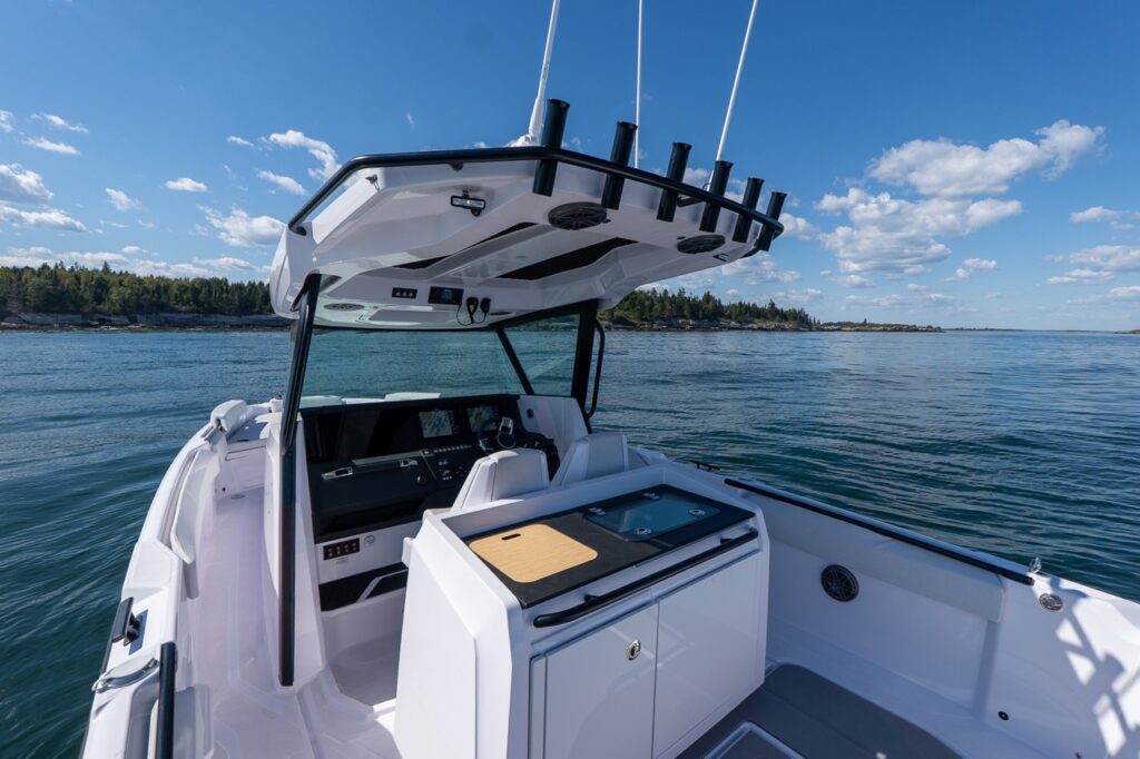 Axopar 29 CCX center console with T-top, rod holders, helm with twin Simrad Multi Function Displays (MFDs), and a tackle station behind the helm on calm coastal water.