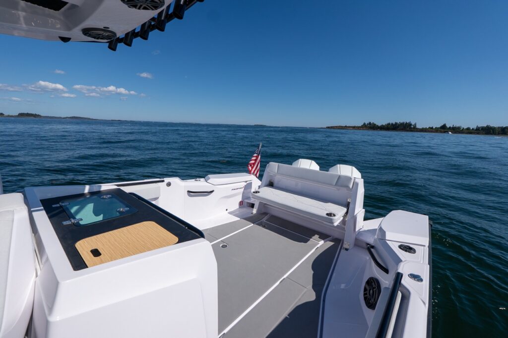 Wide view of the Axopar 29 CCX aft cockpit showing the tackle station module with a teak-style work surface, open aft deck space, and fold-down staple seating at the transom.