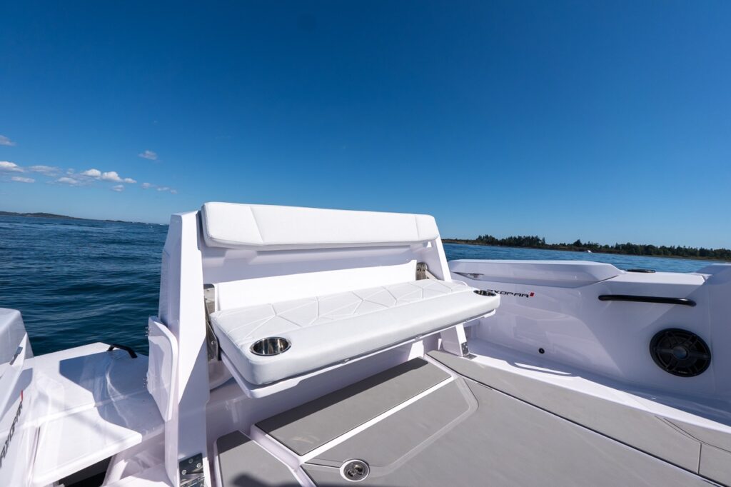 Fold-down staple seating deployed on the aft deck of an Axopar 29 CCX with white upholstery, integrated cupholders, and open water in the background.