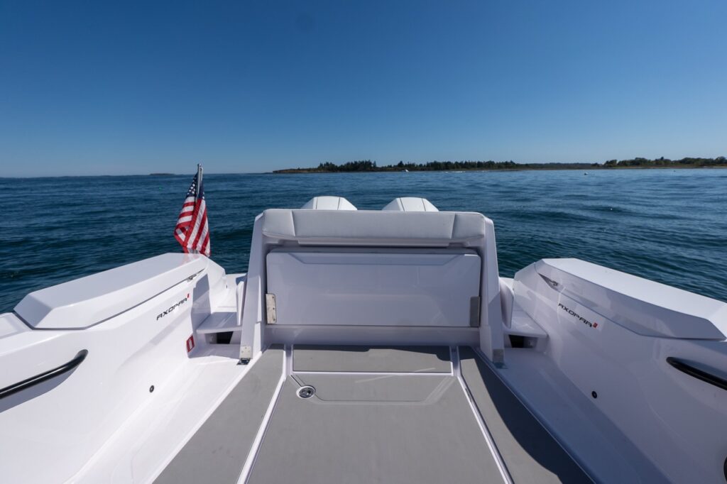 Aft deck of an Axopar 29 CCX with the staple seats folded away and the aft deck storage locker closed, with open water and an American flag in the background.