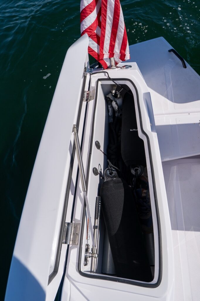 Open fender box on an Axopar 29 CCX showing stored boat fenders beside the aft deck, with an American flag above the transom and water alongside.