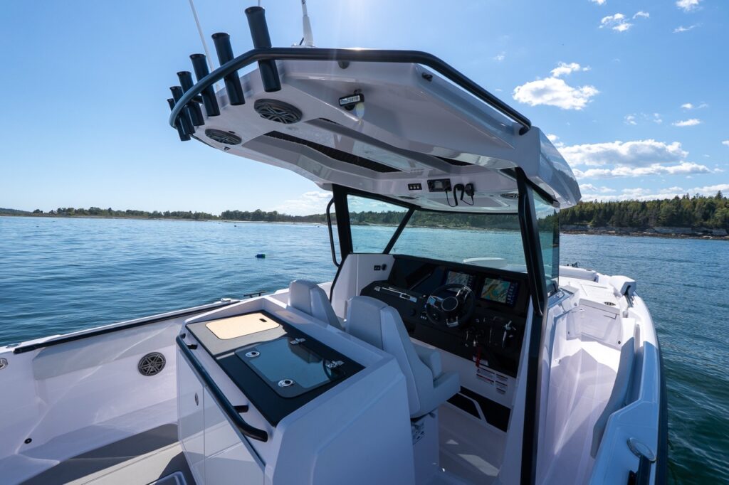 Wide view of the Axopar 29 CCX center console showing the open helm, protective hardtop with rod holders, twin MFDs at the dash, and walkaround side decks in calm coastal water.