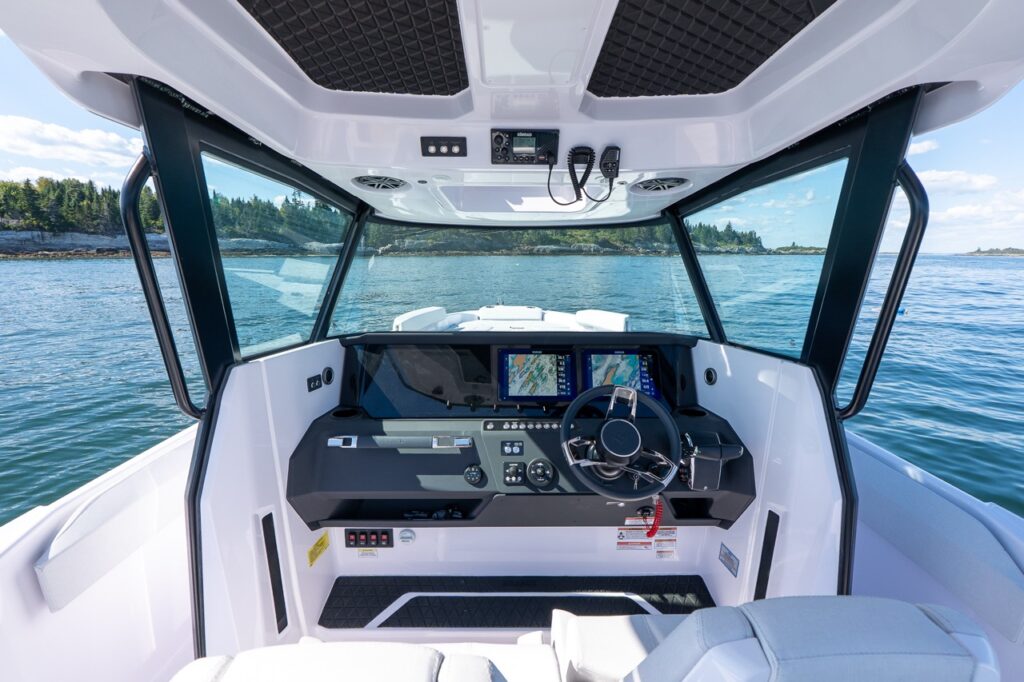 Helm station of the Axopar 29 CCX featuring twin Simrad Multi Function Displays, stainless-trimmed dash, and premium bolster helm seats with panoramic windshield visibility.