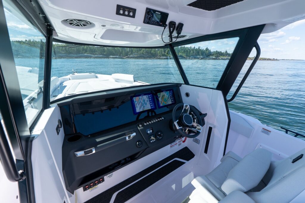 Helm station of the Axopar 29 CCX featuring twin Simrad Multi Function Displays, stainless-trimmed dash, and premium bolster helm seats with panoramic windshield visibility.