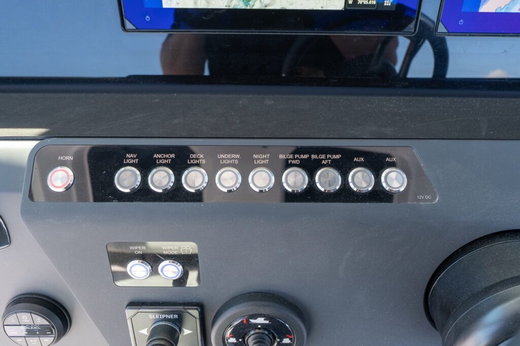 Axopar 29 CCX center console dash switch panel with horn button and labeled push-button controls for navigation lights, anchor light, deck lights, underwater lights, night light, forward and aft bilge pumps, and auxiliary circuits.
