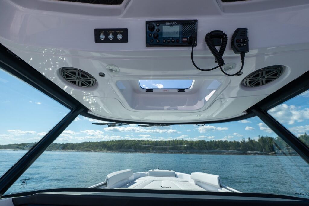Axopar 29 CCX overhead console with Simrad VHF radio, mic, speakers, light switches, and a center skylight above the windshield.