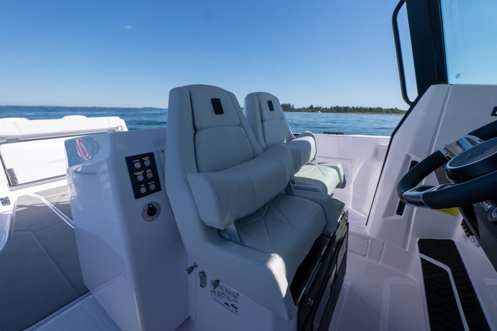 Two cushioned Axopar 29 CCX helm and companion seats with flip-up bolsters and armrests, positioned beside the center console with open water in the background.