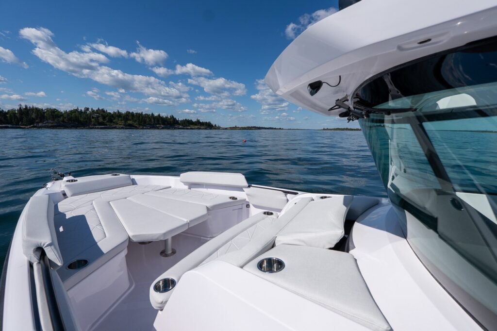 Angled view from the helm area toward the Axopar 29 CCX bow lounge, showing wraparound seating, removable table, and stainless cupholders with open water ahead.