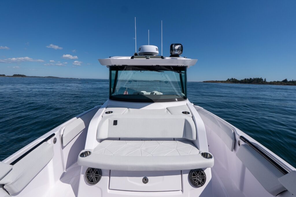 Head-on view of the Axopar 29 CCX center console with forward bow seating, a raised sun pad/backrest, and stainless cupholders on a calm, sunny day.