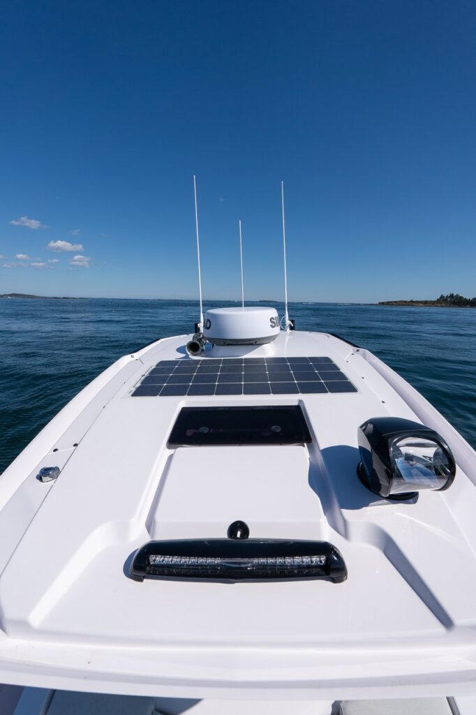 Forward view over the Axopar 29 CCX roof showing a flush solar panel, Simrad radar dome with antennas, and a roof-mounted spotlight above the open water.