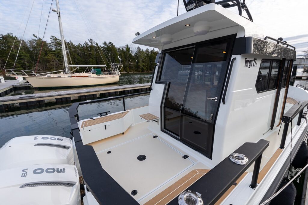 Aft deck view of a Targa 27.2 Coupe at the dock, highlighting the wide swim platform, twin Mercury outboards, secure railings, teak-style decking, and pilothouse sliding glass door.