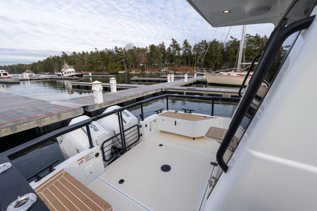 Aft cockpit view of a Targa 27.2 Coupe at the dock, showing the wide cockpit sole, teak-style decking, secure railings, integrated aft seating, and twin Mercury outboards.