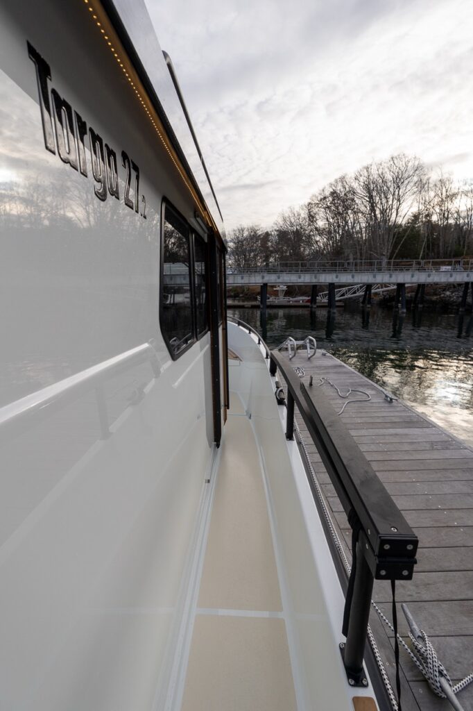 Starboard side deck of a Targa 27.2 Coupe at the dock, showing wide walkaround passage, non-skid deck surface, tall safety rail, and pilothouse side windows with integrated roof lighting.