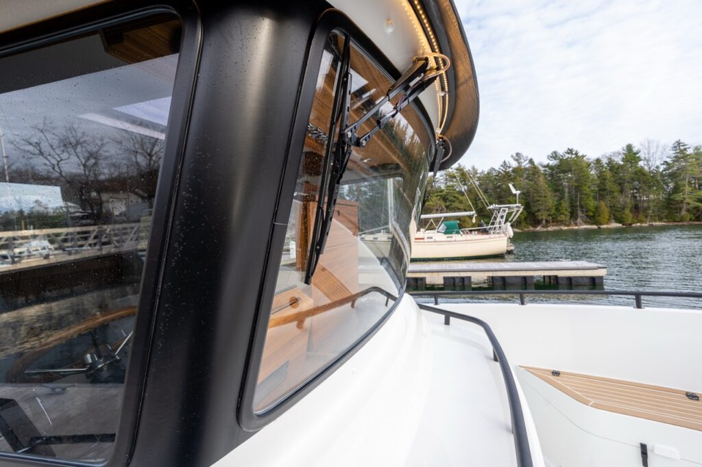 Close-up of the Targa 27.2 Coupe pilothouse front corner, showing opening windshield section, heavy-duty window framing, integrated roof lighting, and secure foredeck rail.