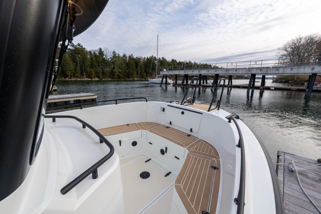 Forward deck area of a Targa 27.2 Coupe at the dock, showing wraparound seating with teak-style surfaces, deep deck well, non-skid flooring, and high protective railings.