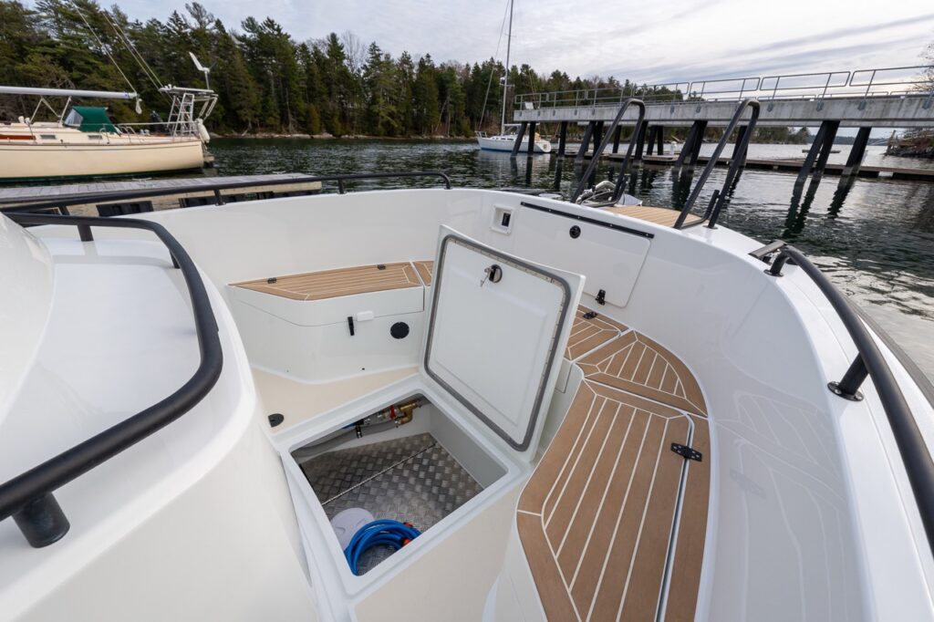 Forward deck area of a Targa 27.2 Coupe with an open deck hatch, showing deep molded storage below, teak-style deck surfaces, non-skid flooring, and high surrounding rails.