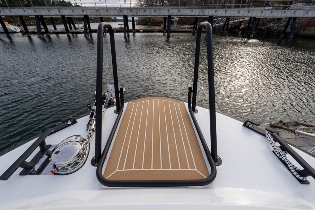Foredeck of a Targa 27.2 Coupe at the dock, showing the teak-style center walkway, tall twin handrails, flush-mounted anchor windlass, and secure deck hardware.