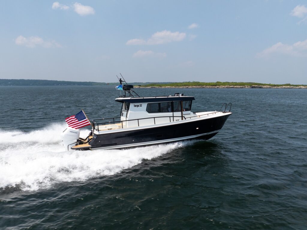 A Targa 32 pilothouse boat running at speed on open water, shown broadside with twin Mercury outboards and a U.S. flag flying off the stern.