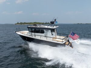 A Targa 32 pilothouse boat running at speed on open water, viewed from aft-quarter, with twin Mercury outboards creating a strong wake and an American flag flying at the stern.
