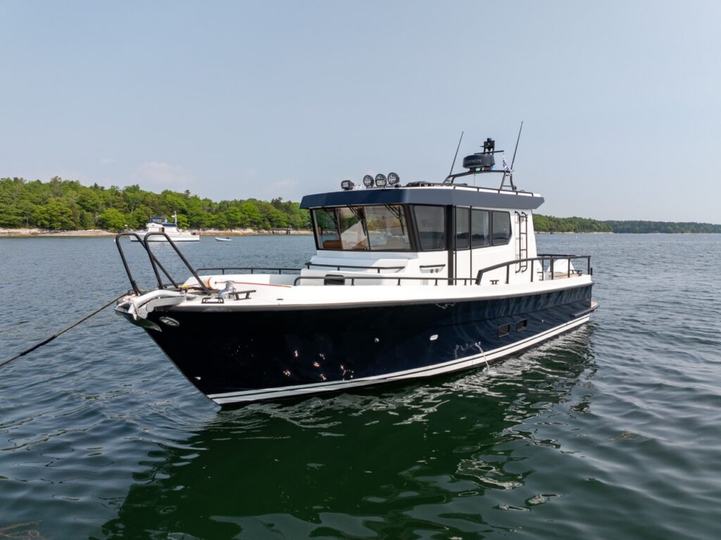Three-quarter bow view of a Targa 32 pilothouse boat floating on calm coastal water, showing the sharp bow, black hull, enclosed wheelhouse, and walkaround decks.