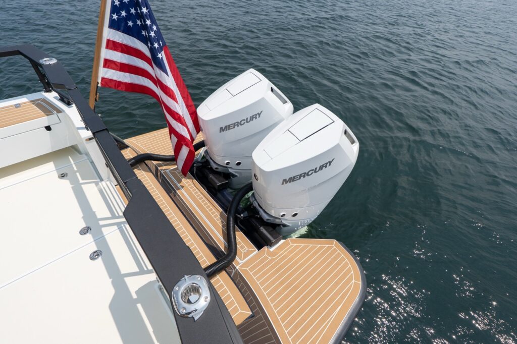 Twin white Mercury Verado outboards mounted on the stern of a Targa 32, viewed from above with teak-style swim platforms and an American flag flying over calm water.