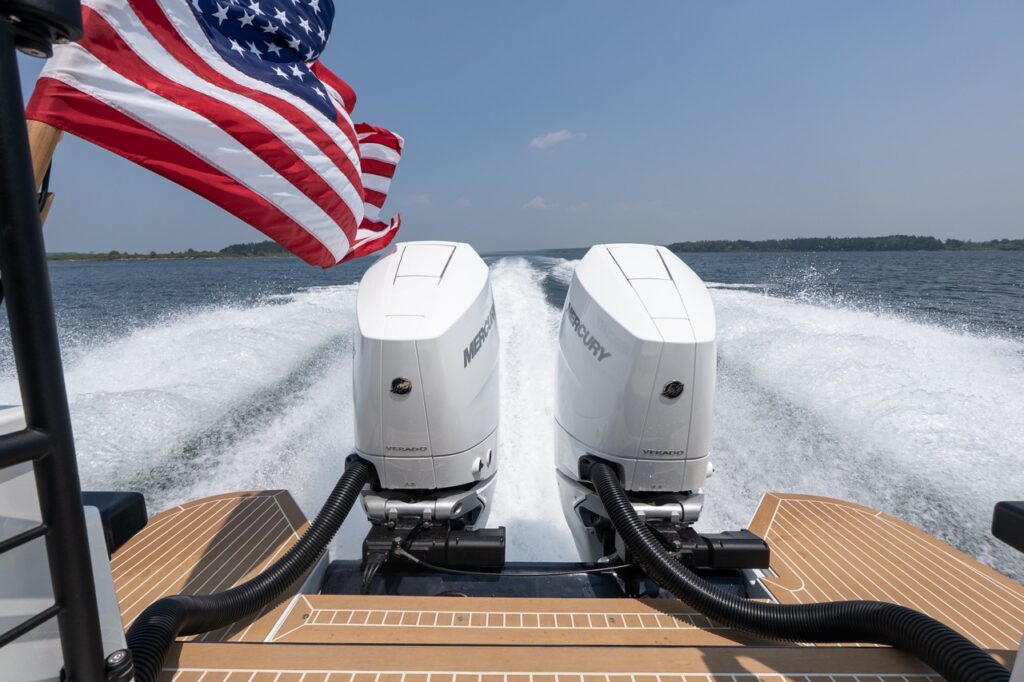Twin Mercury Verado outboard engines powering a Targa 32 at speed, with a U.S. flag flying above and a clean wake spreading across open water.