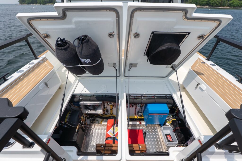 Dual aft deck hatches open on a Targa 32, revealing symmetrical machinery compartments with fuel systems, electrical equipment, safety gear, and aluminum tread plate flooring.