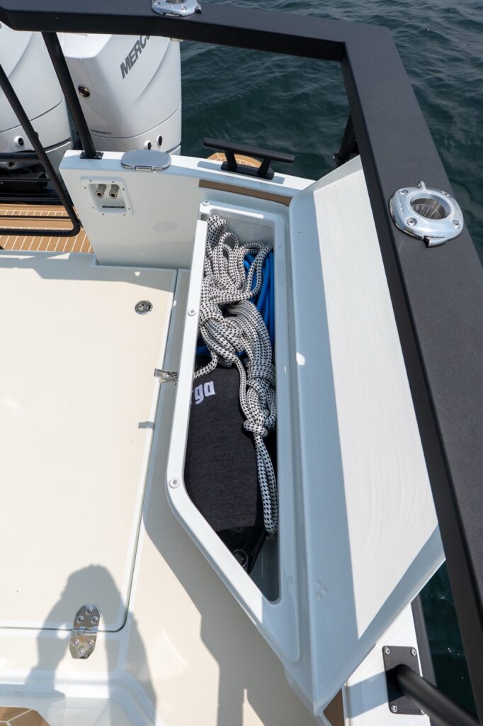 Narrow aft cockpit side locker on a Targa 32 with the lid open, showing coiled dock lines and a blue washdown hose neatly stowed beside the transom.