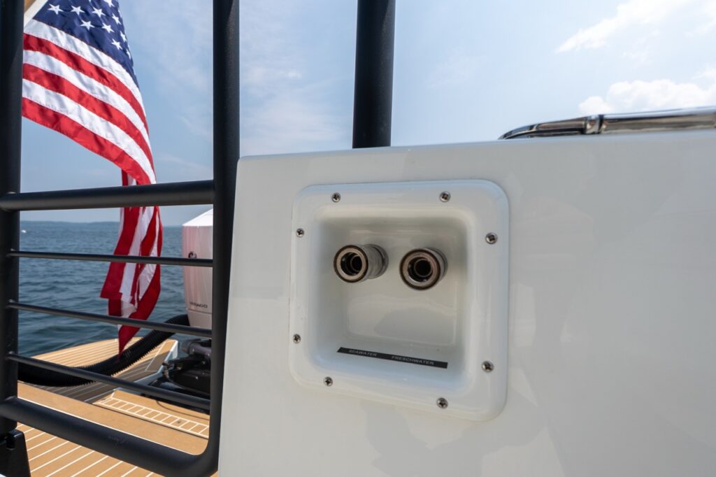 Close-up of the aft washdown connection panel on a Targa 32, showing dedicated seawater and freshwater outlets at the stern with the American flag and open water behind.