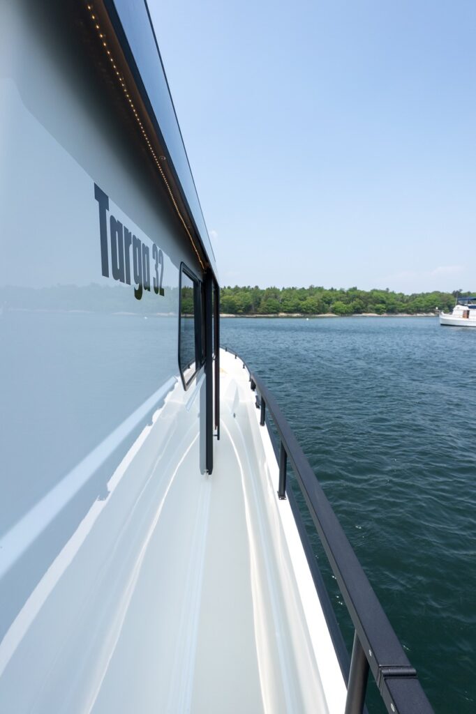 Starboard side deck walkway on a Targa 32, showing the wide, protected side deck with black handrail, pilothouse windows, and the Targa 32 logo along the cabin side.