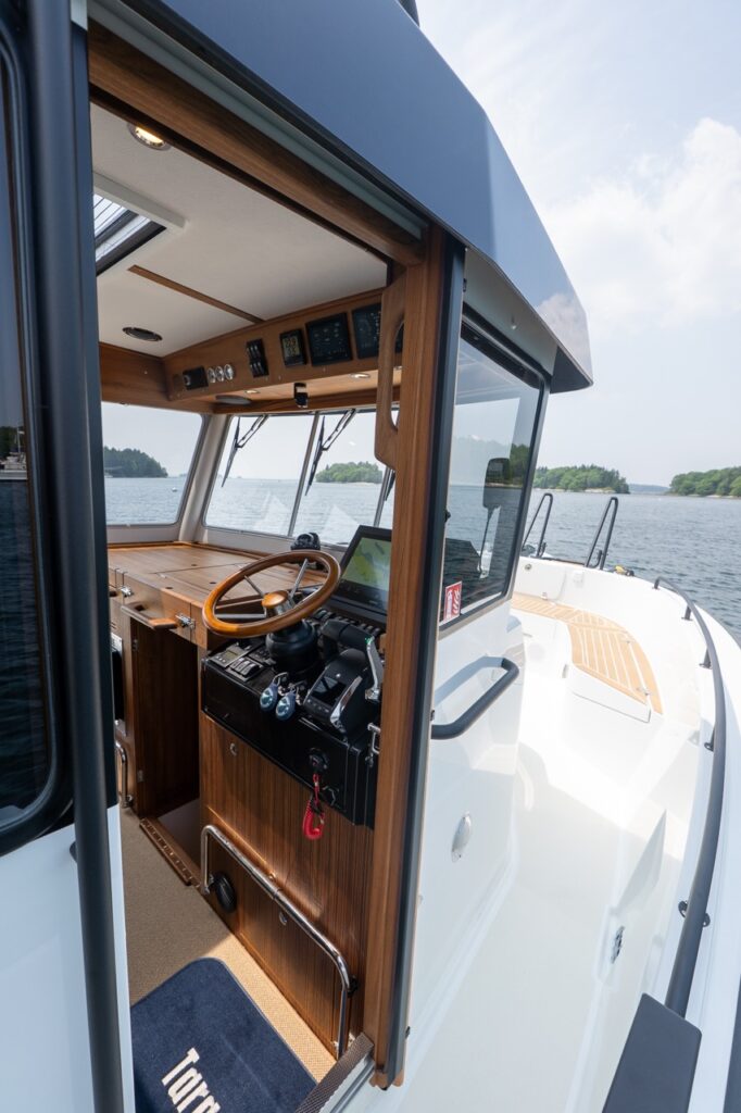 Open sliding helm door on the Targa 32 showing the teak-accented helm station with wooden steering wheel, Garmin displays, and direct access to the starboard side deck.