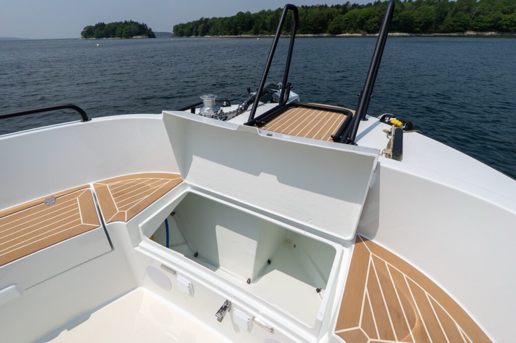 Open forward deck locker on the Targa 32 with the lid raised, revealing a large, clean, molded storage compartment beneath the foredeck, surrounded by teak decking and black safety rails.