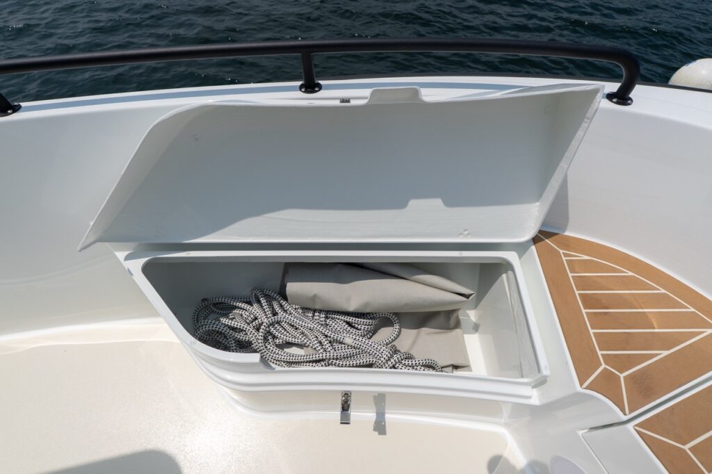 Open bow storage locker on the Targa 32 showing molded white compartment with coiled dock lines inside, set into the foredeck with teak decking alongside.