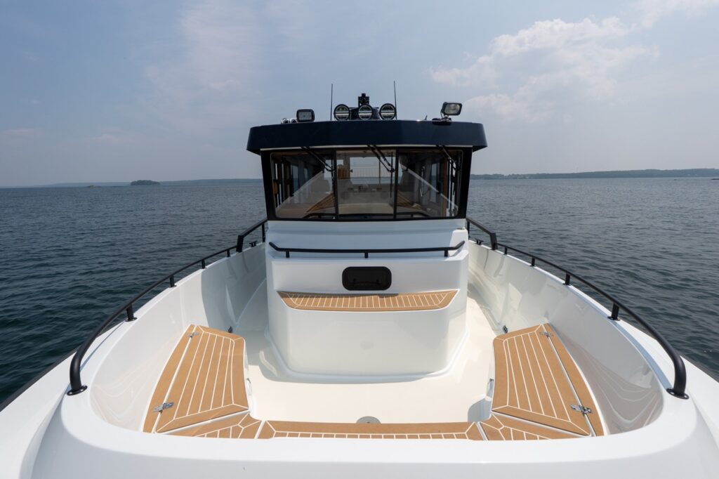Forward cockpit view of the Targa 32 showing twin teak-inlaid seating areas on port and starboard, high bulwarks, and the pilothouse windshield ahead, surrounded by open water.