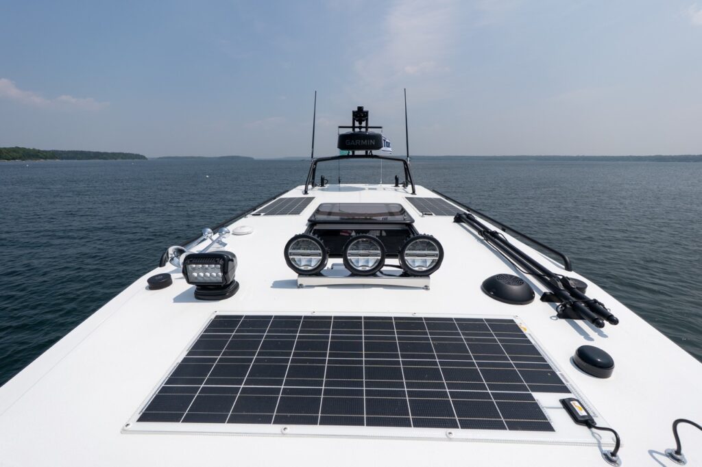 Forward-facing view over the Targa 32 foredeck showing integrated solar panels, roof-mounted LED searchlights, deck hardware, and a Garmin radar dome, with open water ahead.