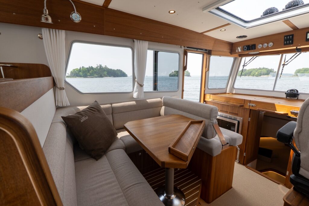 Targa 32 pilothouse interior with port-side dinette seating, teak dining table, large side windows, and the helm area visible forward.
