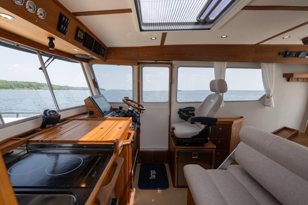 Targa 32 pilothouse interior with helm station, galley countertop, sliding side door, adjustable helm seat, and upholstered settee, surrounded by large windows with open-water views.