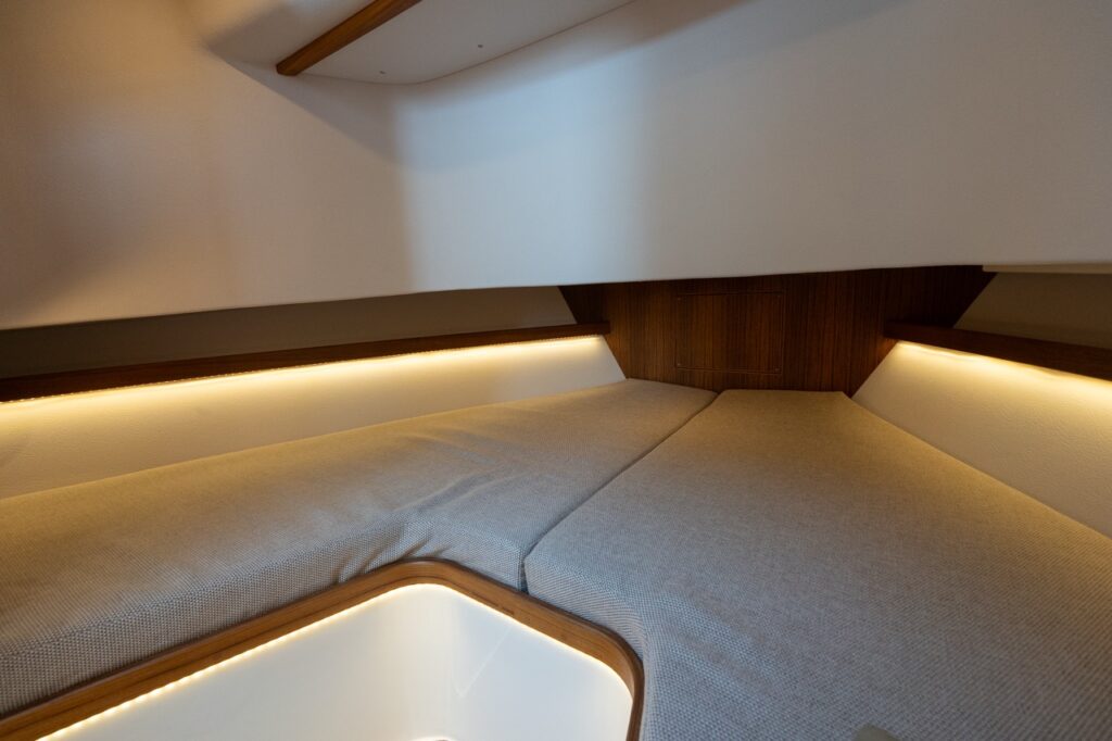 Forward V-berth in the Targa 32’s forward cabin, showing twin cushions, warm indirect LED lighting, and teak trim in a compact sleeping space.