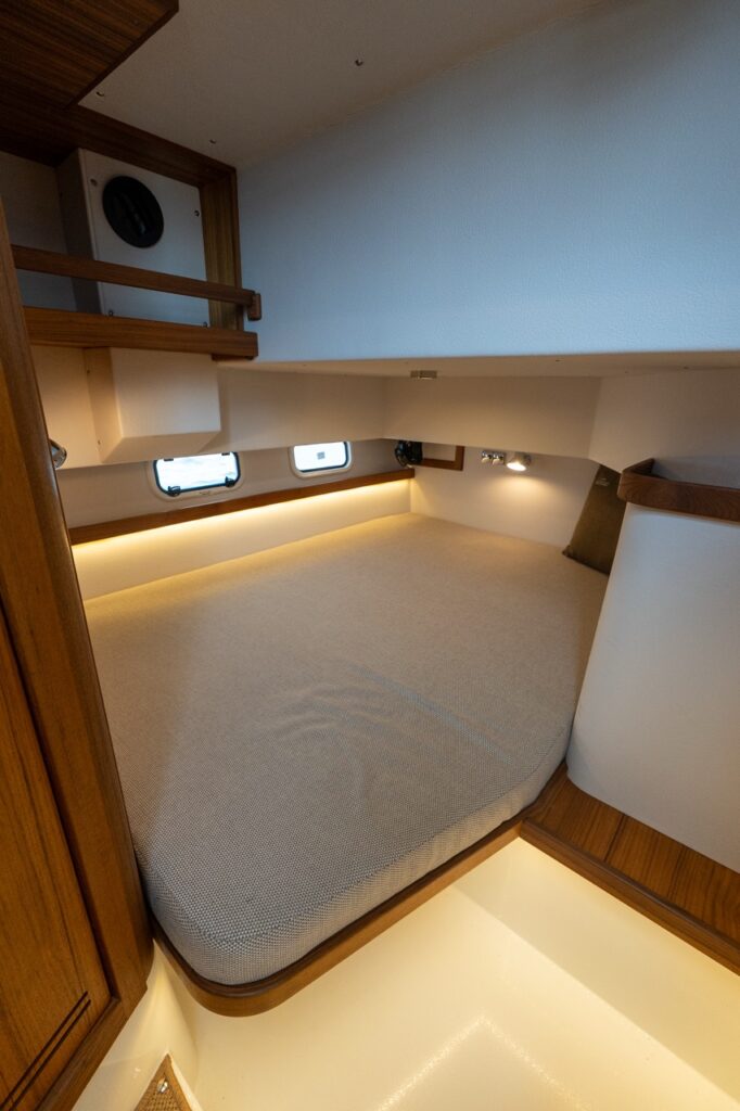Double aft berth on the Targa 32 showing a wide upholstered mattress with rounded corners, teak trim, integrated shelving, reading lights, LED accent lighting, and opening portlights.