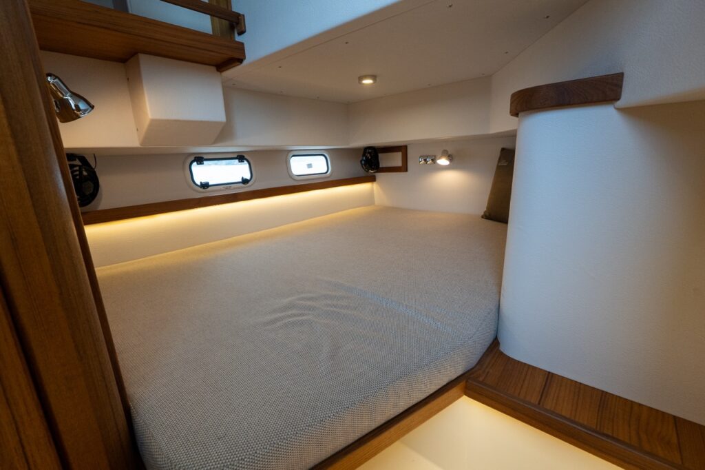 Double aft berth aboard the Targa 32 with a wide upholstered mattress, teak trim, reading lights, LED accent lighting, and multiple opening portlights.