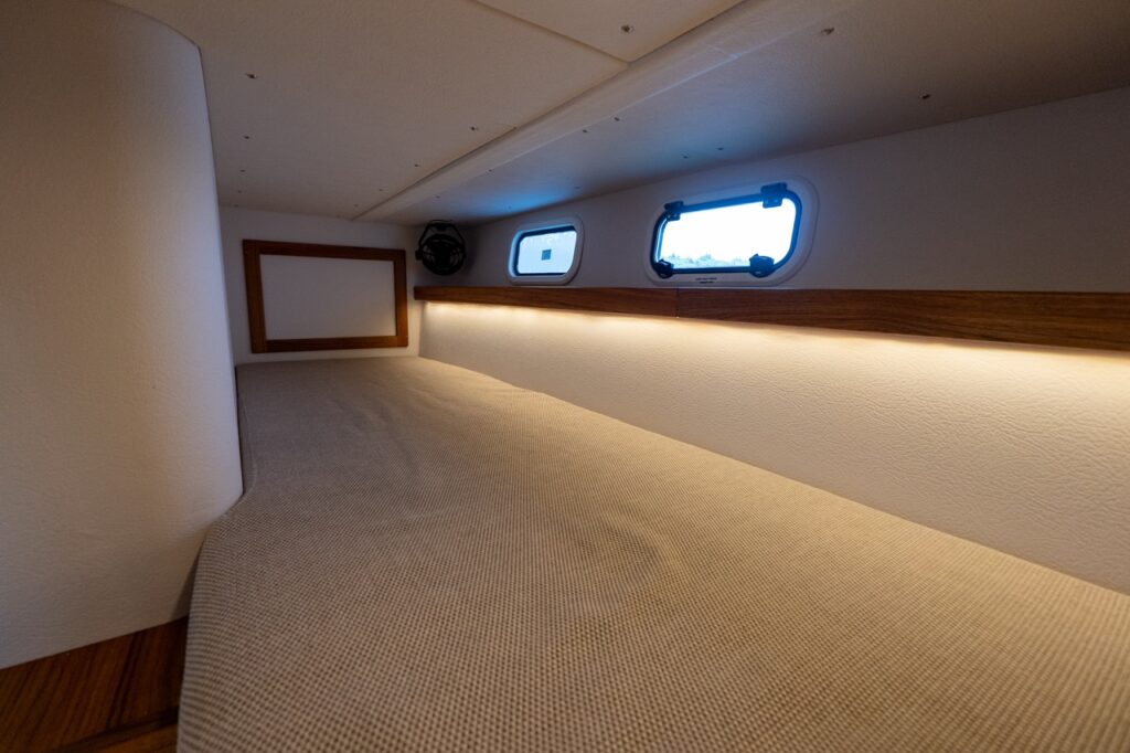 Single aft berth aboard the Targa 32 with upholstered sleeping surface, warm teak trim, soft LED accent lighting, and two opening portlights.