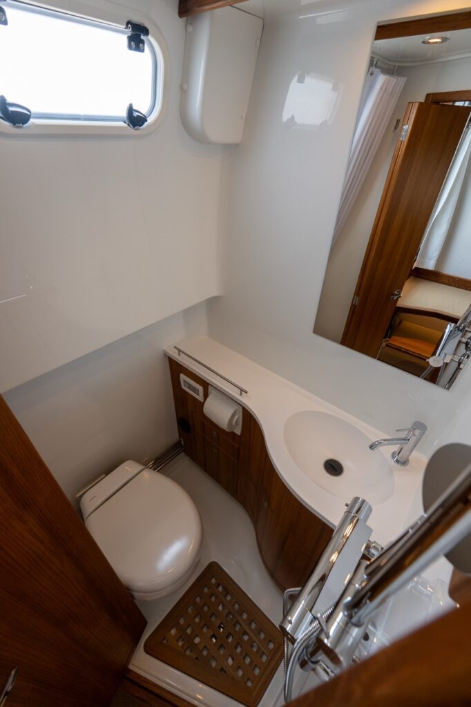 Compact marine head with toilet, molded sink and vanity, chrome faucet, teak accents, mirror, and opening portlight aboard a Targa 32.