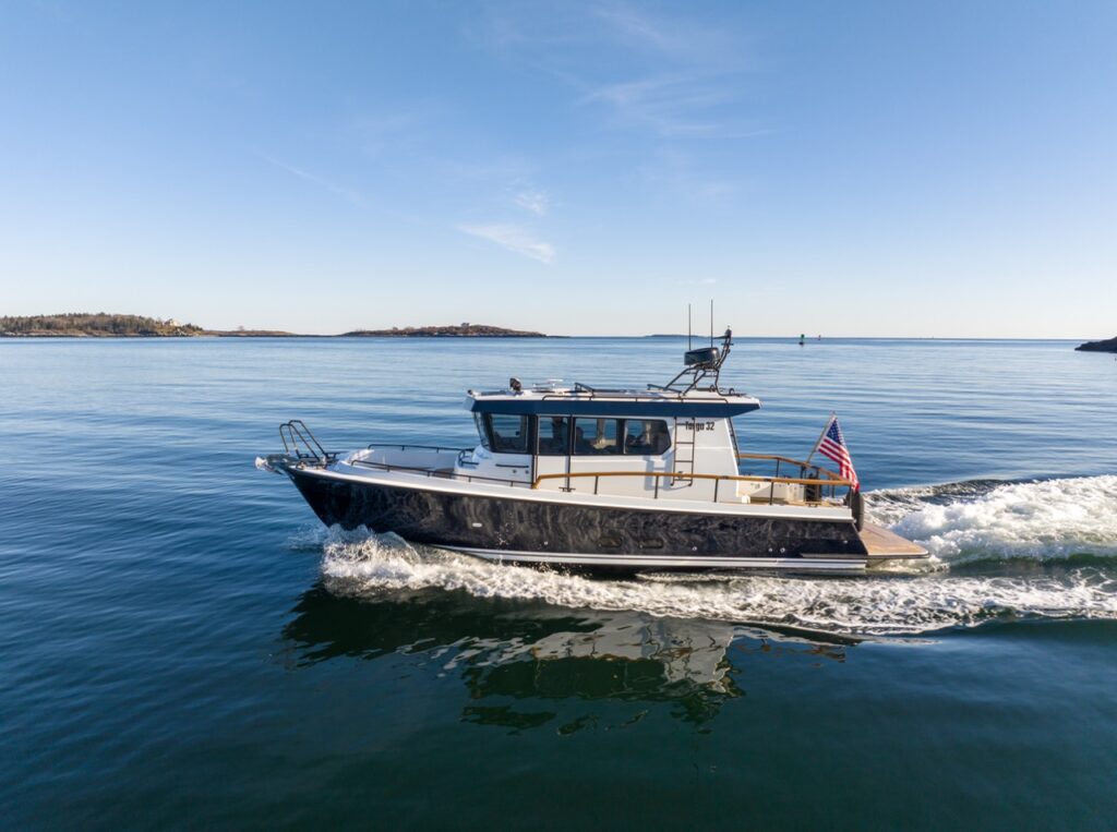 Side profile of a Targa 32 underway on calm coastal water in daylight, leaving a gentle wake with the American flag flying at the stern and islands in the distance.