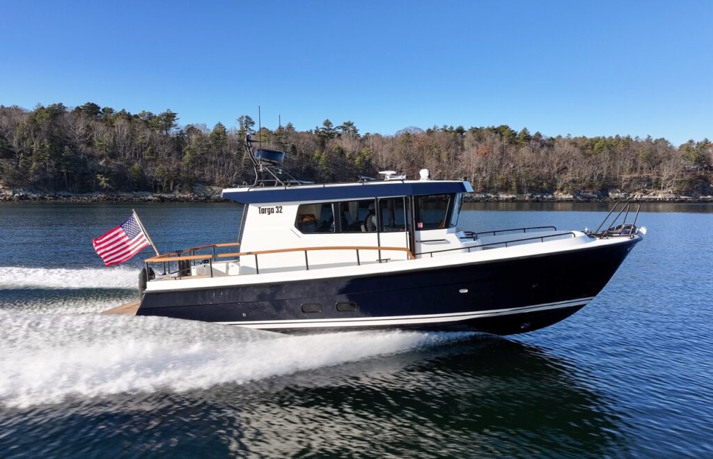 Targa 32 cruising at speed in daylight, seen in profile with an American flag flying aft, dark hull cutting cleanly through calm coastal water.